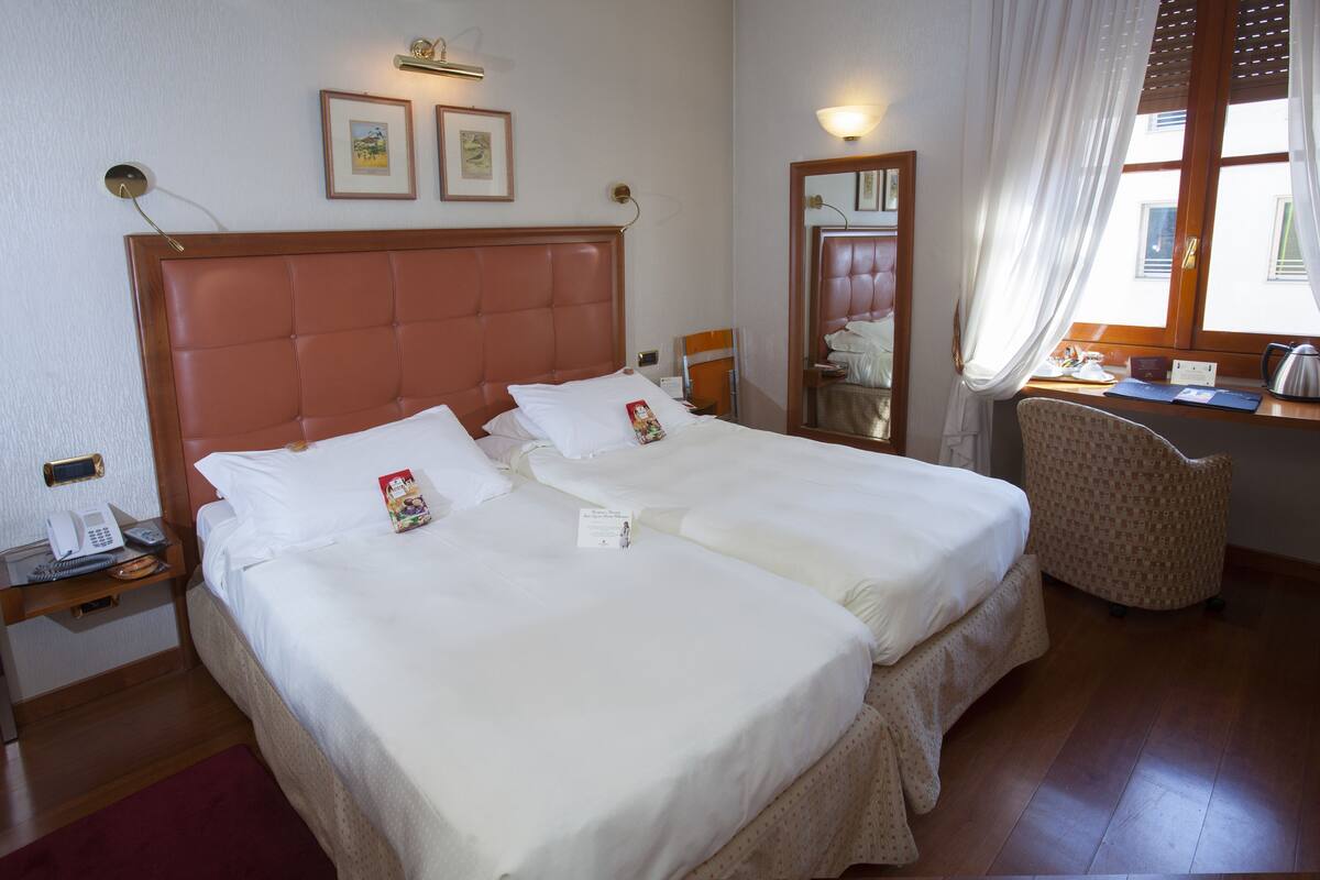 A double bed with white linens, a bedside table with a phone, and a chair.