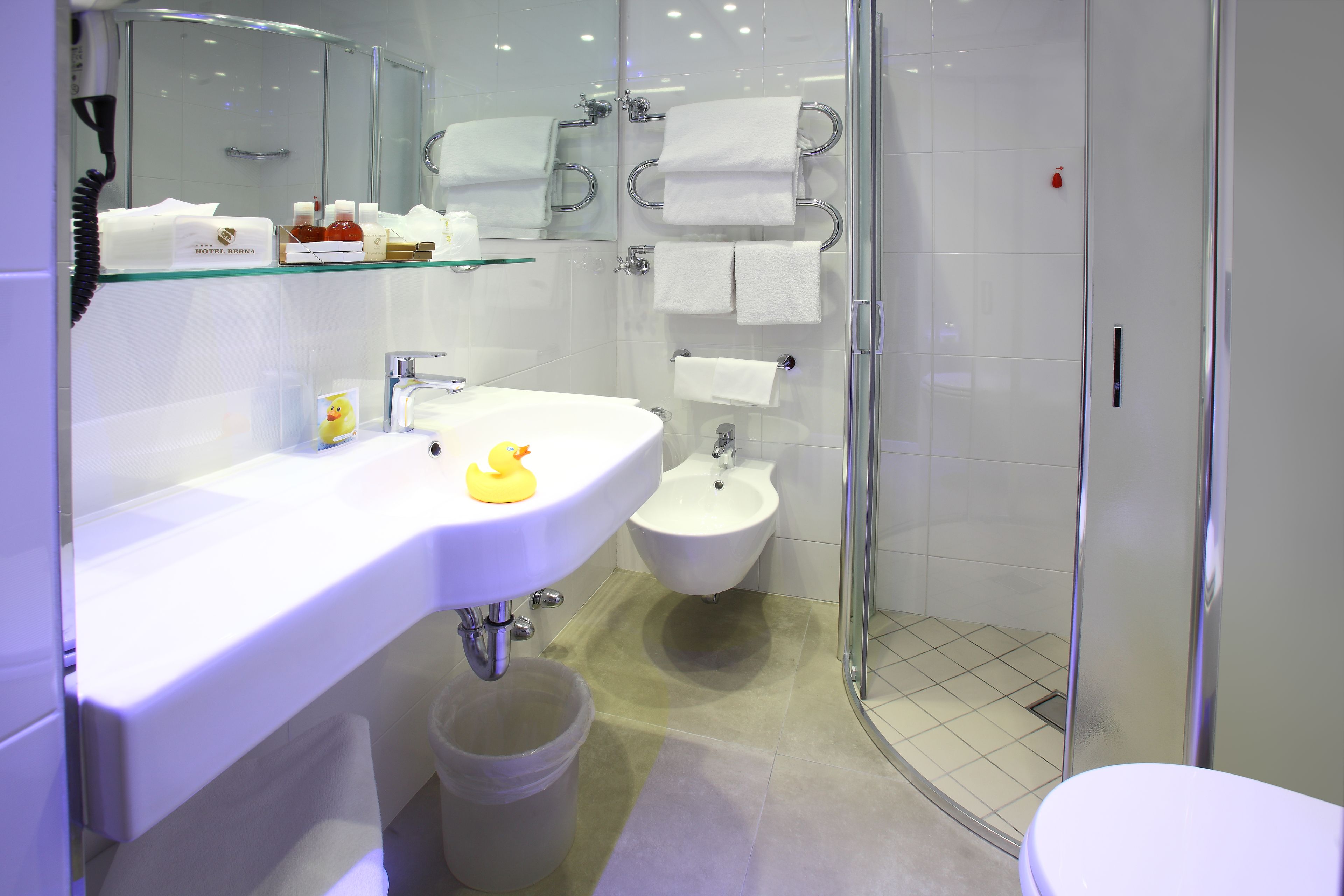 Een moderne badkamer met een douchecabine van glas, een witte wastafel met een rubberen eend en een douchetoilet.