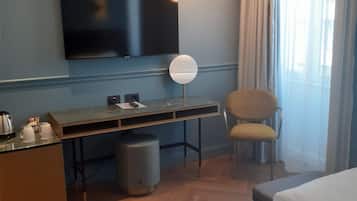 A hotel room with a flat-screen TV mounted on the wall, a desk with a lamp, a chair, and two beds.