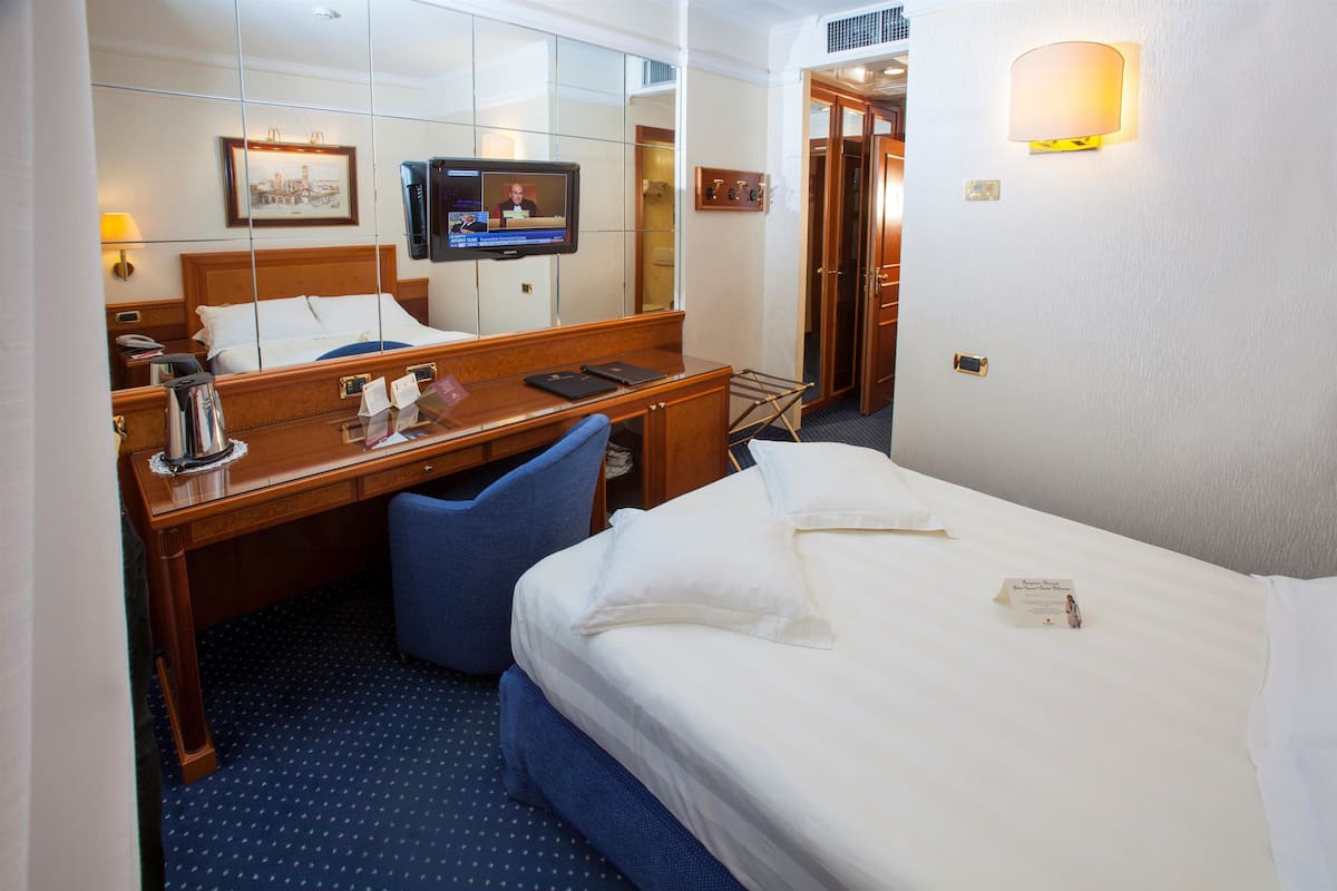 A hotel room with a bed, a desk, a chair, a TV, and a mirror.