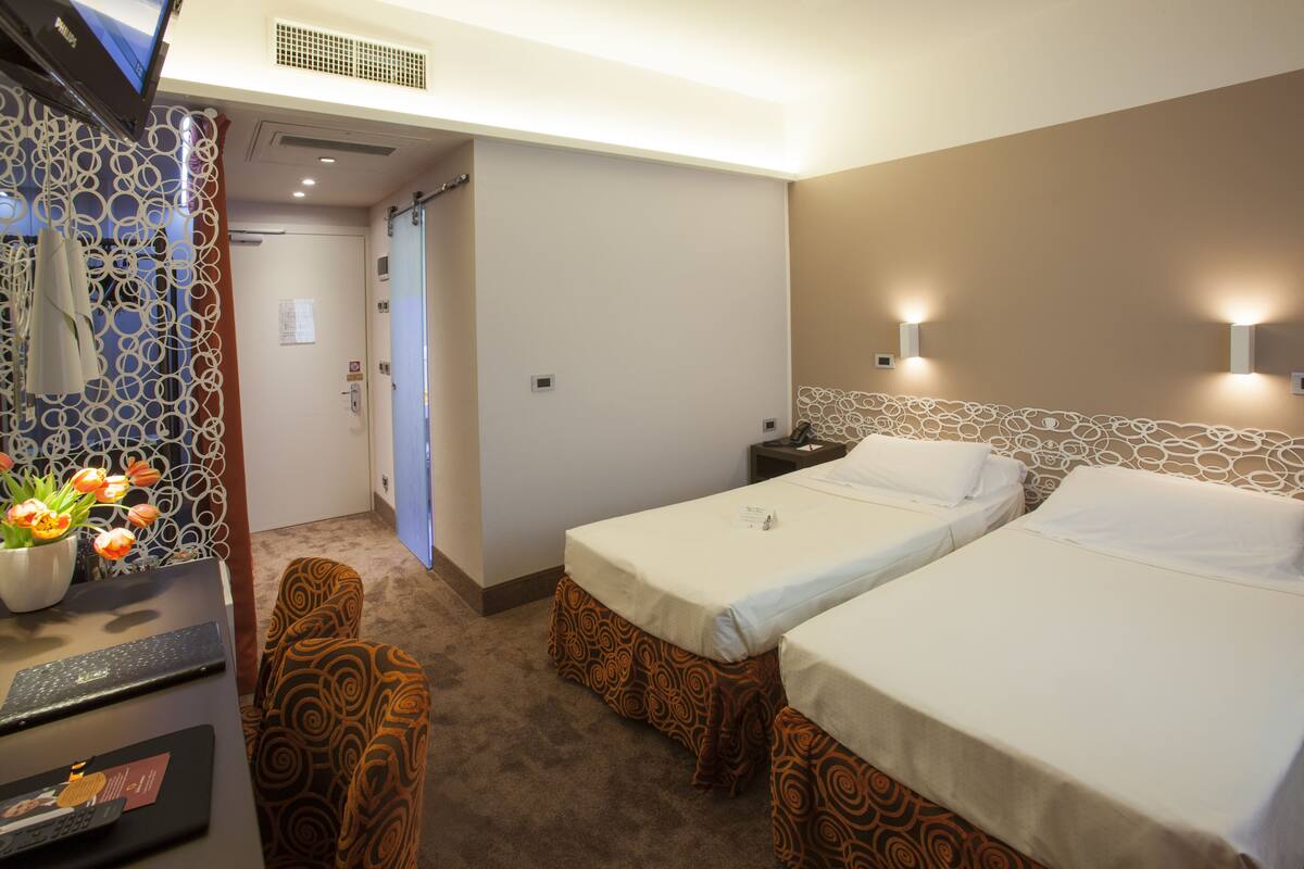 A hotel room with two beds, a desk with a computer, a TV, and a decorative wall.