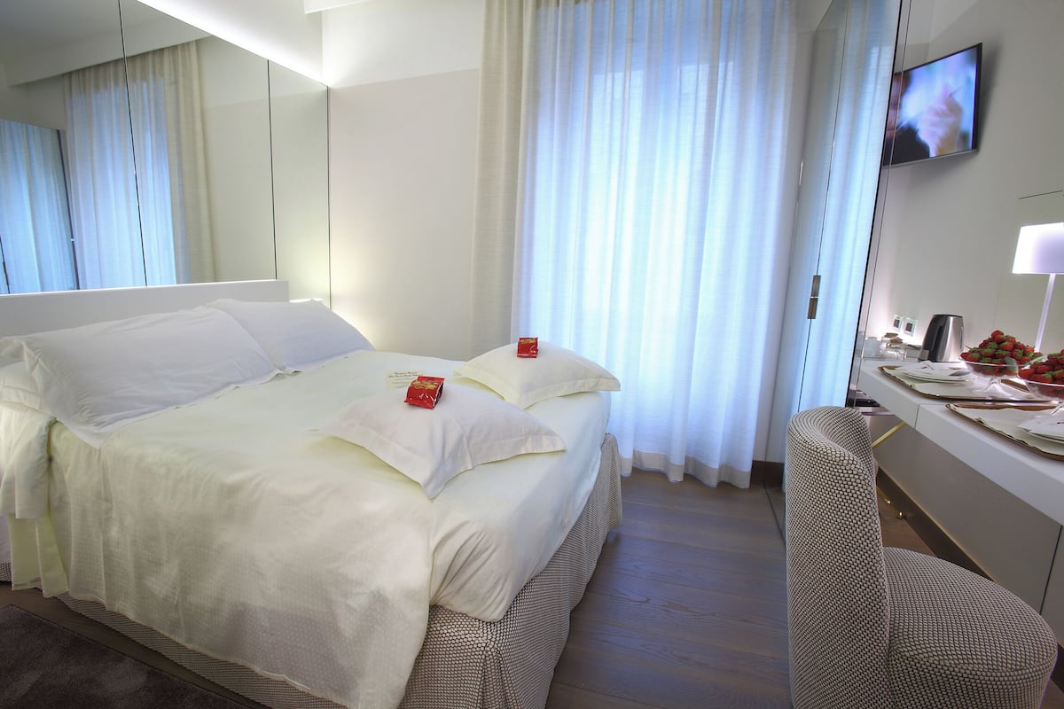 A hotel room with a large bed, a desk with a chair, a television, and a window with curtains.