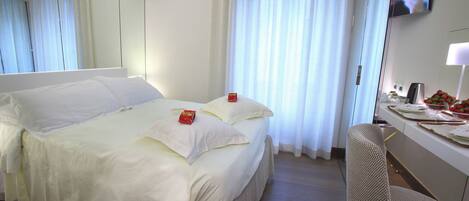 A hotel room with a large bed, a desk with a chair, a television, and a window with curtains.