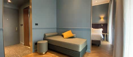 A modern hotel room with a sofa bed, a small round ottoman, and a wooden floor.