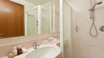 Un baño con ducha de azulejos de mármol, un lavabo blanco y un espejo encima.