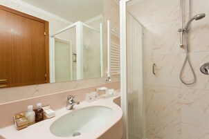 Un baño con ducha de azulejos de mármol, un lavabo blanco y un espejo encima.
