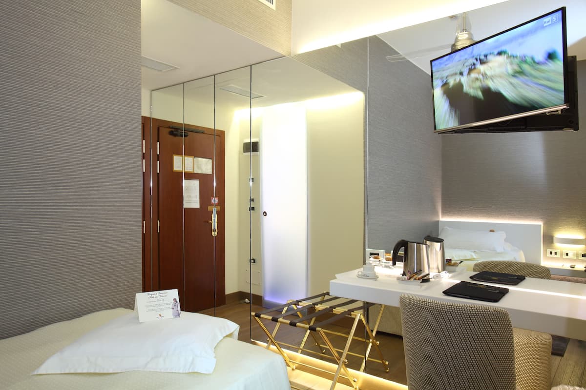 A hotel room with a bed, a desk with a flat-screen TV, a chair, and a mirror.