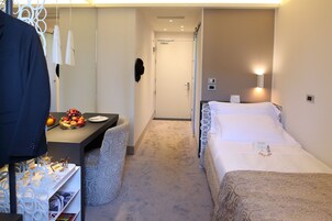 A hotel room with two beds, a desk with a fruit bowl, a coat rack, and a small table with magazines.