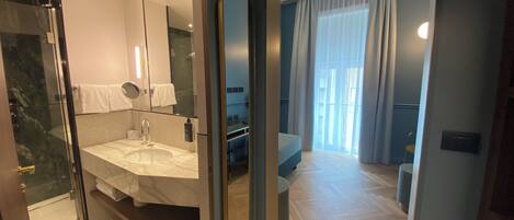 Un baño moderno con cabina de ducha de vidrio, un espejo grande y un mueble de tocador con lavamanos y toallero.