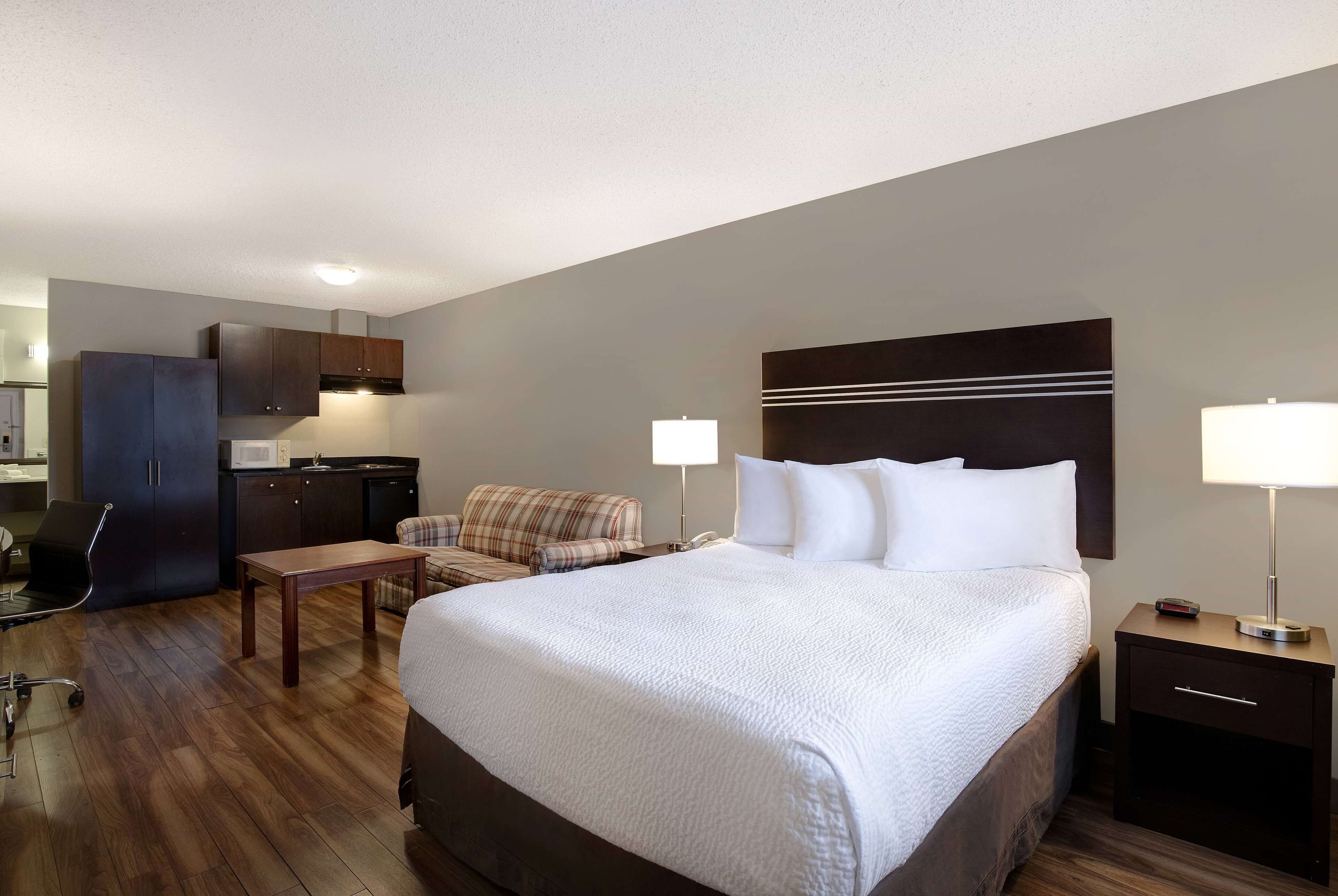 Hotelkamer met een groot bed, een bureau, een stoel, een bank, een kledingkast en een nachtkastje met een lamp.