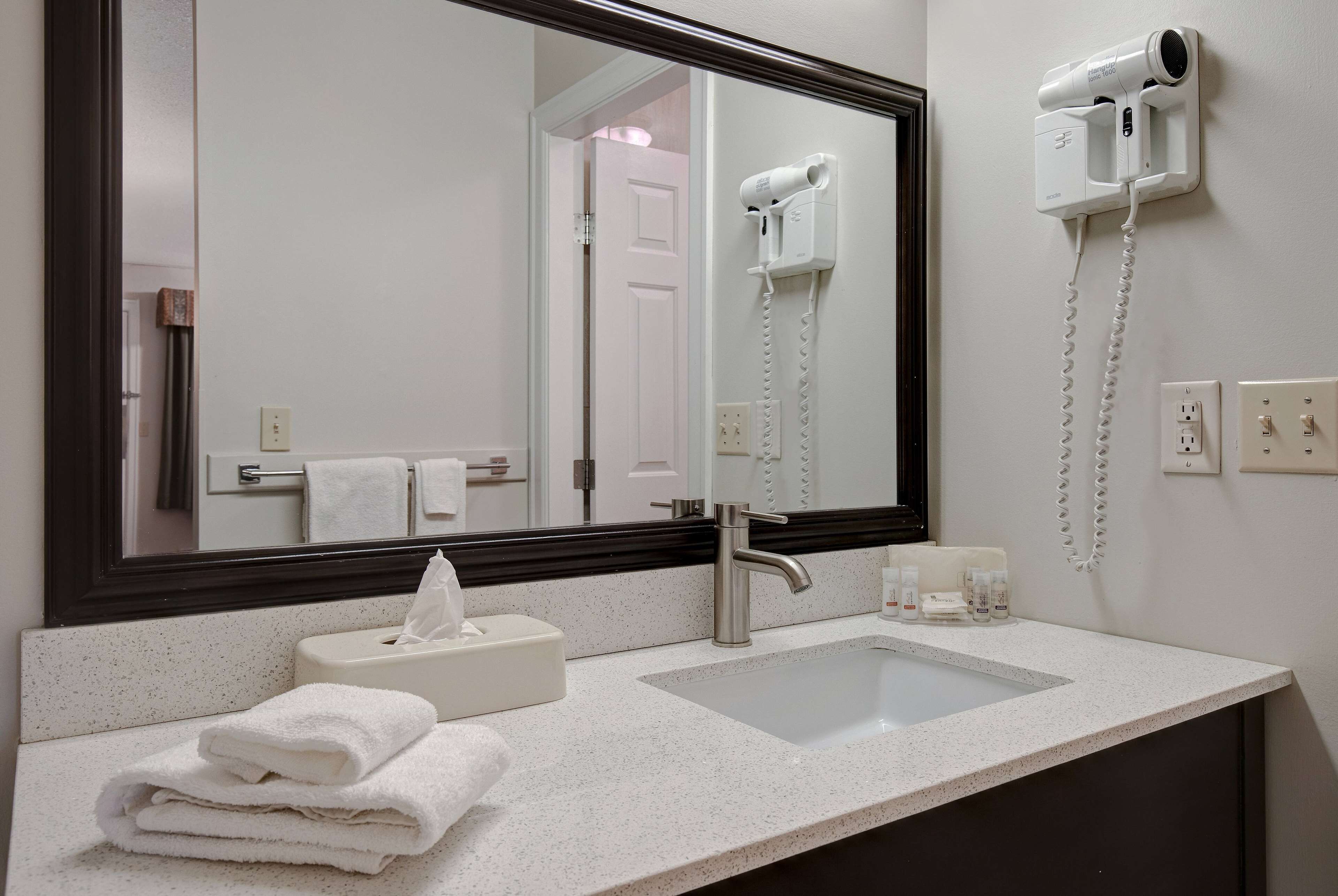 A bathroom with a sink, mirror, and hair dryer mounted on the wall.