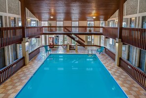 An indoor swimming pool with a wooden deck, multiple levels with railings, and a view of the outside through large windows. - Days Inn by Wyndham Vernon (Vernon)