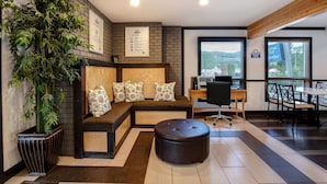 A modern hotel lobby with a sectional sofa, a large potted plant, a round ottoman, a desk with a computer, and a dining area with chairs and tables. - Days Inn by Wyndham Vernon (Vernon)