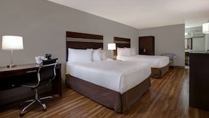 A hotel room with two beds, a desk with a chair, and a kitchenette. - Days Inn by Wyndham Vernon (Vernon)