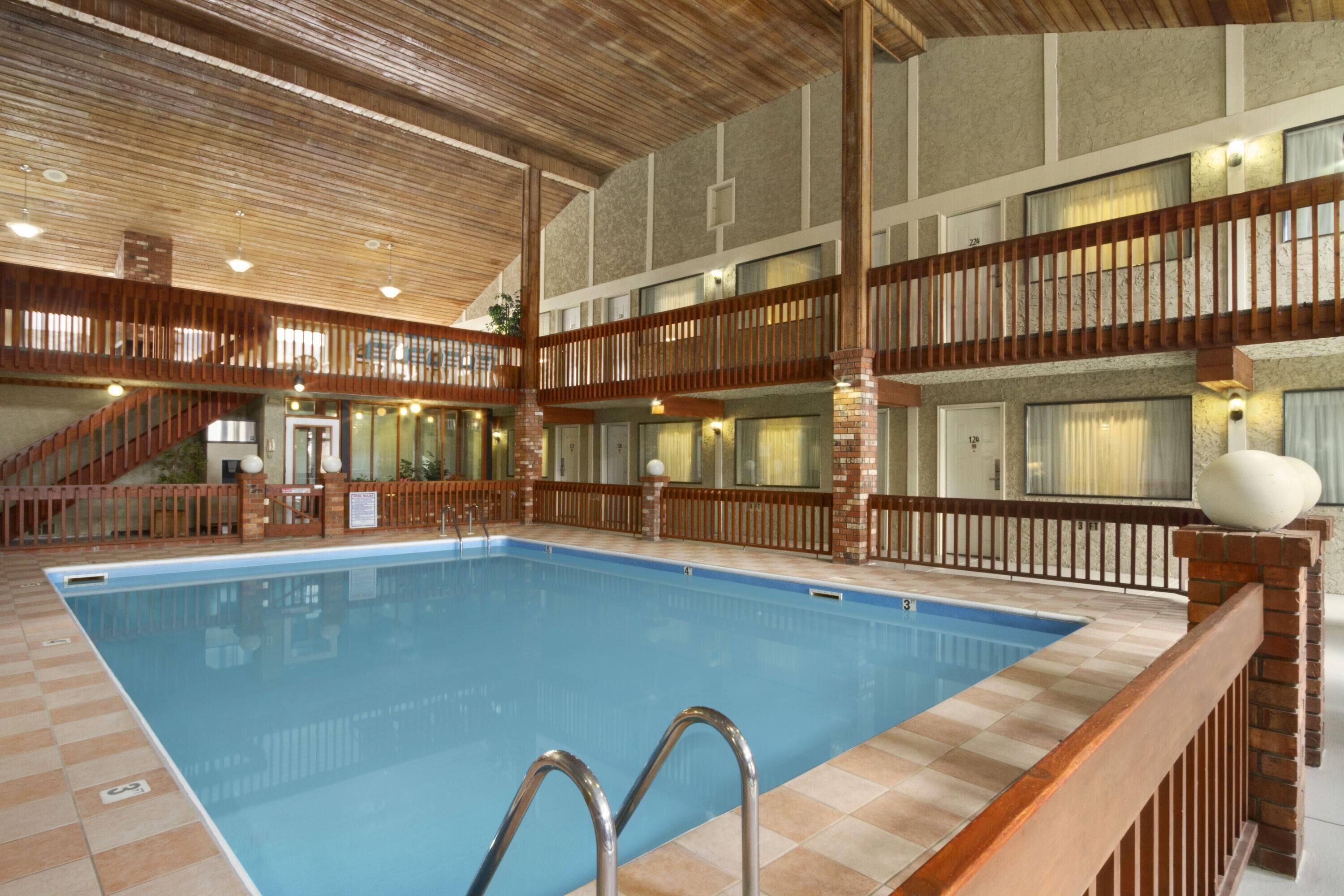 A large indoor swimming pool with a wooden deck surrounding it, multiple balconies, and a staircase leading to upper levels.