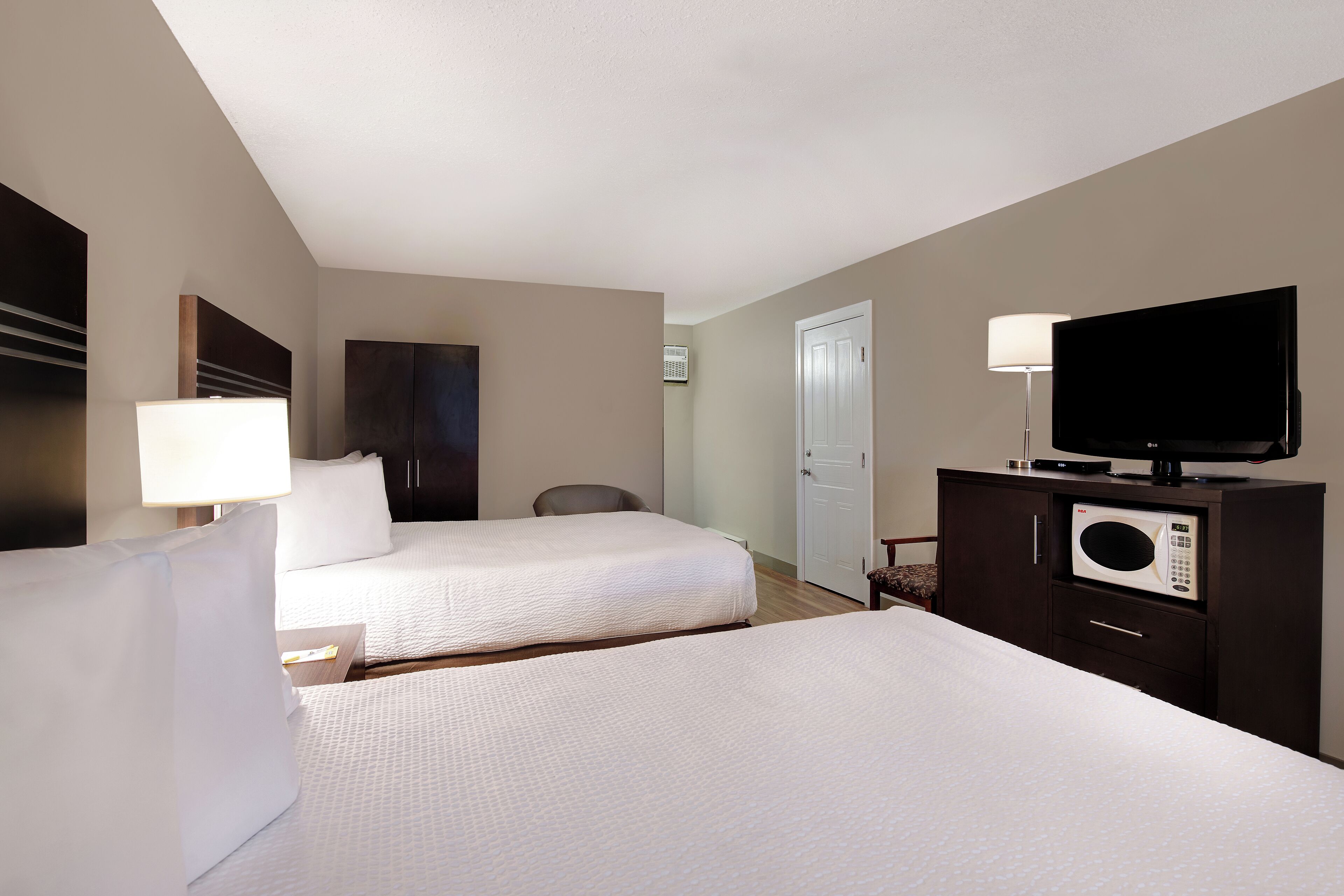 A hotel room with two beds, a flat-screen TV, a microwave, and a desk lamp.