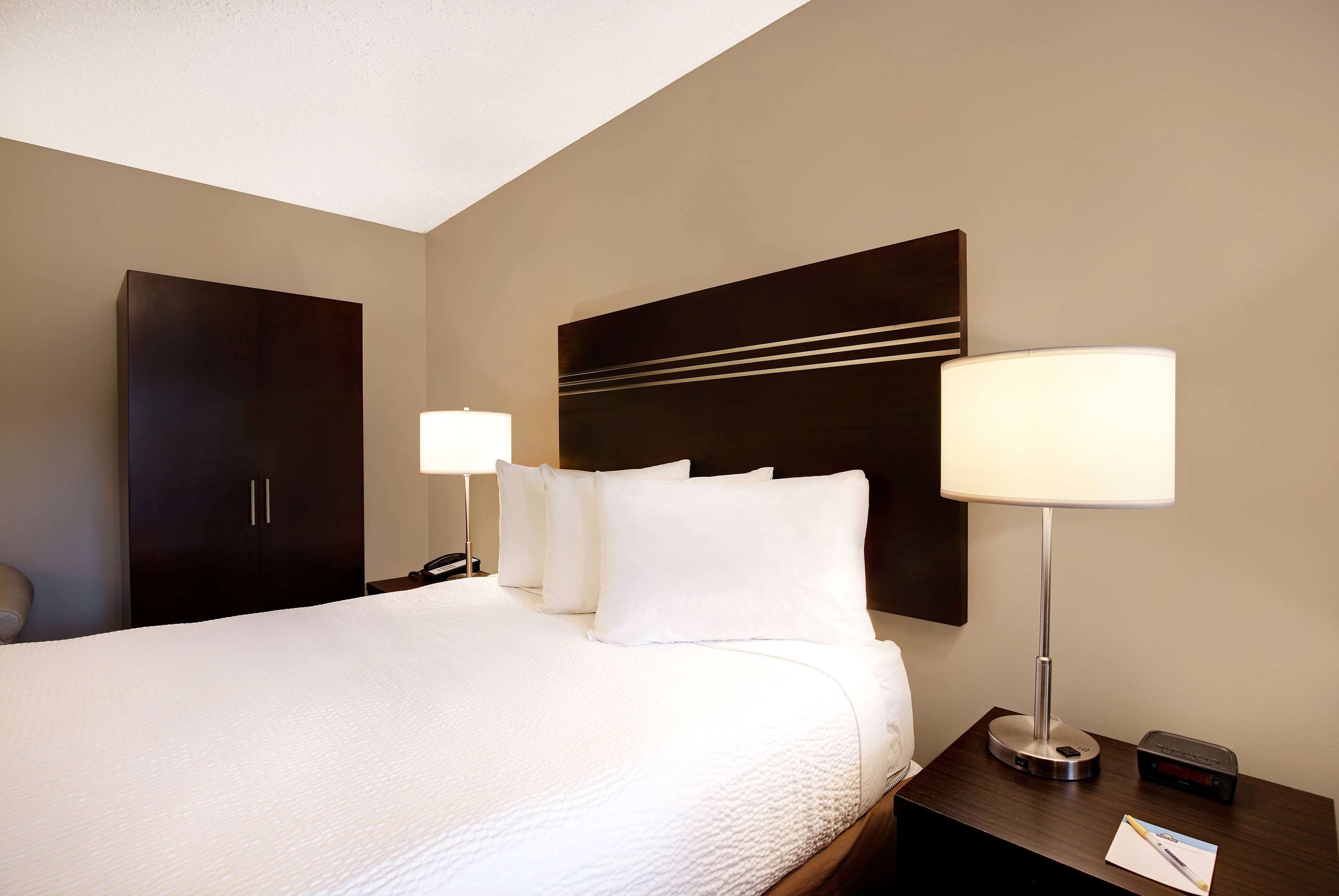 A hotel room with a large bed, two bedside lamps, a nightstand, and a dark-colored wardrobe.