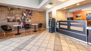 Un espace d’accueil d’hôtel avec une pancarte « Bienvenue », un comptoir de réception, une machine à café et des sièges.