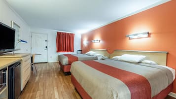 A hotel room with two beds, a TV, a desk with a lamp, and a bathroom.