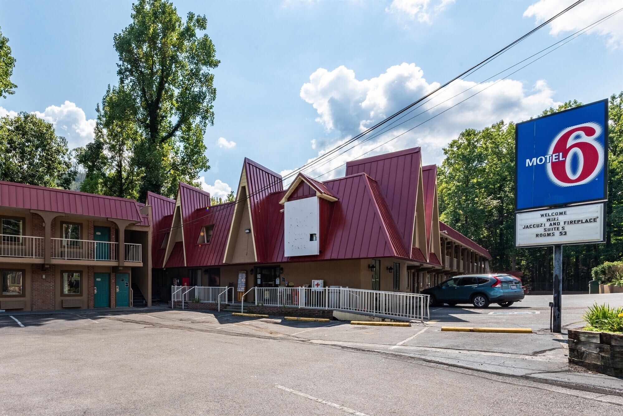 Un motel à l’esthétique particulière, avec une combinaison de couleurs rouge et beige, qui se distingue par un grand panneau représentant le chiffre « 6 » et un panneau d’accueil indiquant la présence de suites avec jacuzzi et cheminée.