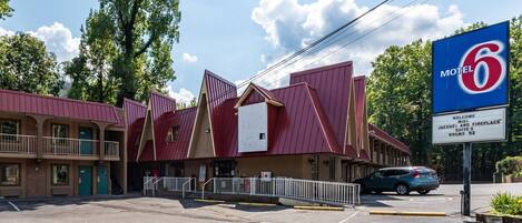 Un motel à l’esthétique particulière, avec une combinaison de couleurs rouge et beige, qui se distingue par un grand panneau représentant le chiffre « 6 » et un panneau d’accueil indiquant la présence de suites avec jacuzzi et cheminée.