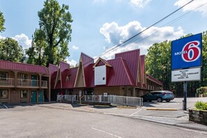 Een motel met een opvallend rood-beige kleurenschema, met een groot bord met het cijfer '6' en een verwelkomingsbord voor suites met jacuzzi en open haard.