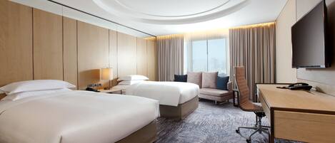 A hotel room with two beds, a desk, a chair, a TV, and a large window with curtains.