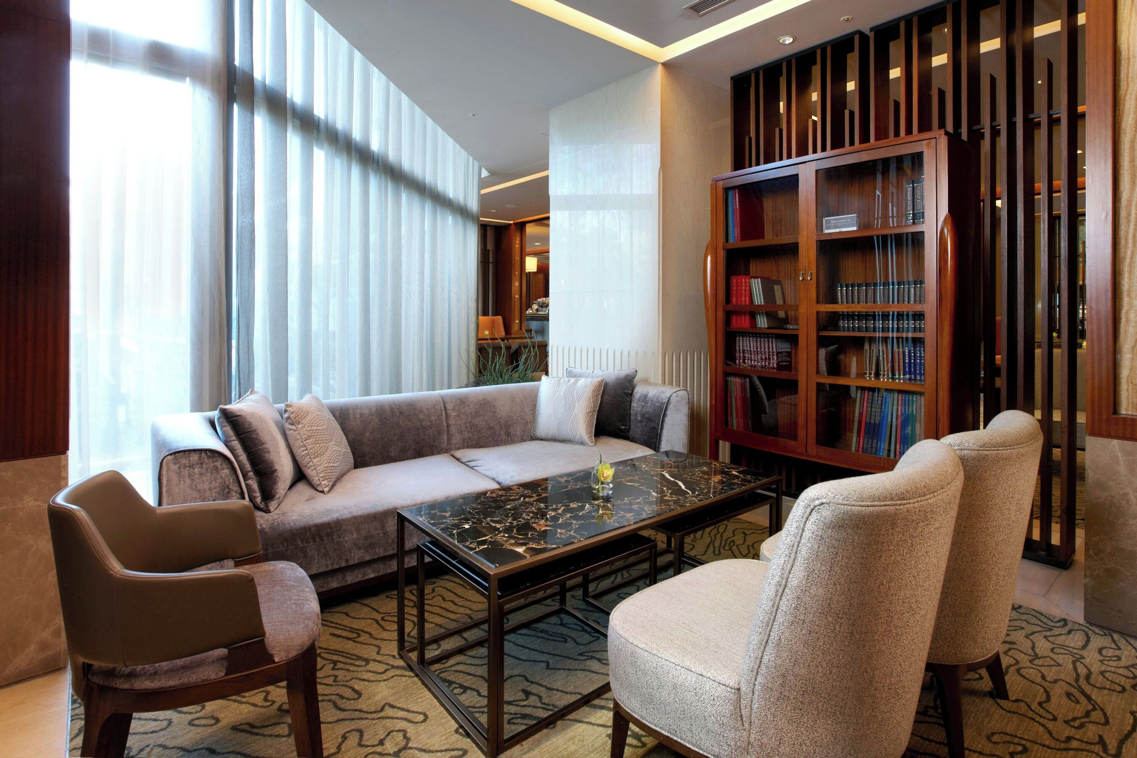 Een moderne woonkamer met een bank, fauteuils, een salontafel en een boekenkast.