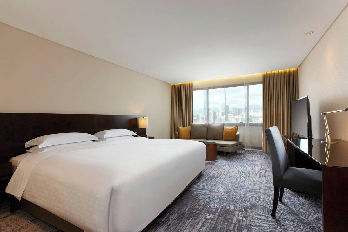 A hotel room with a large bed, a sofa, a desk, and a TV.