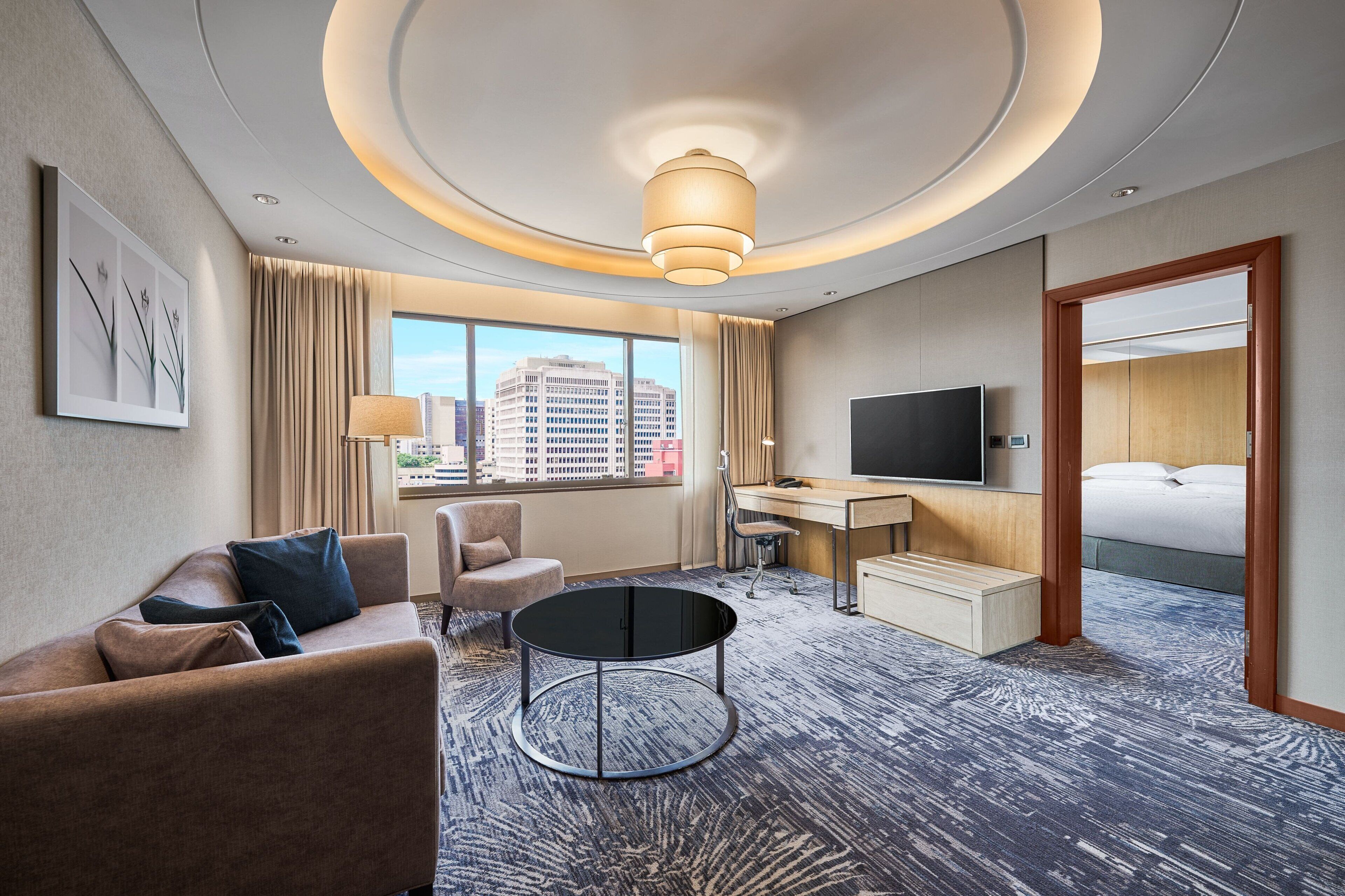 A hotel room with a sofa, armchair, desk, TV, and a bed.