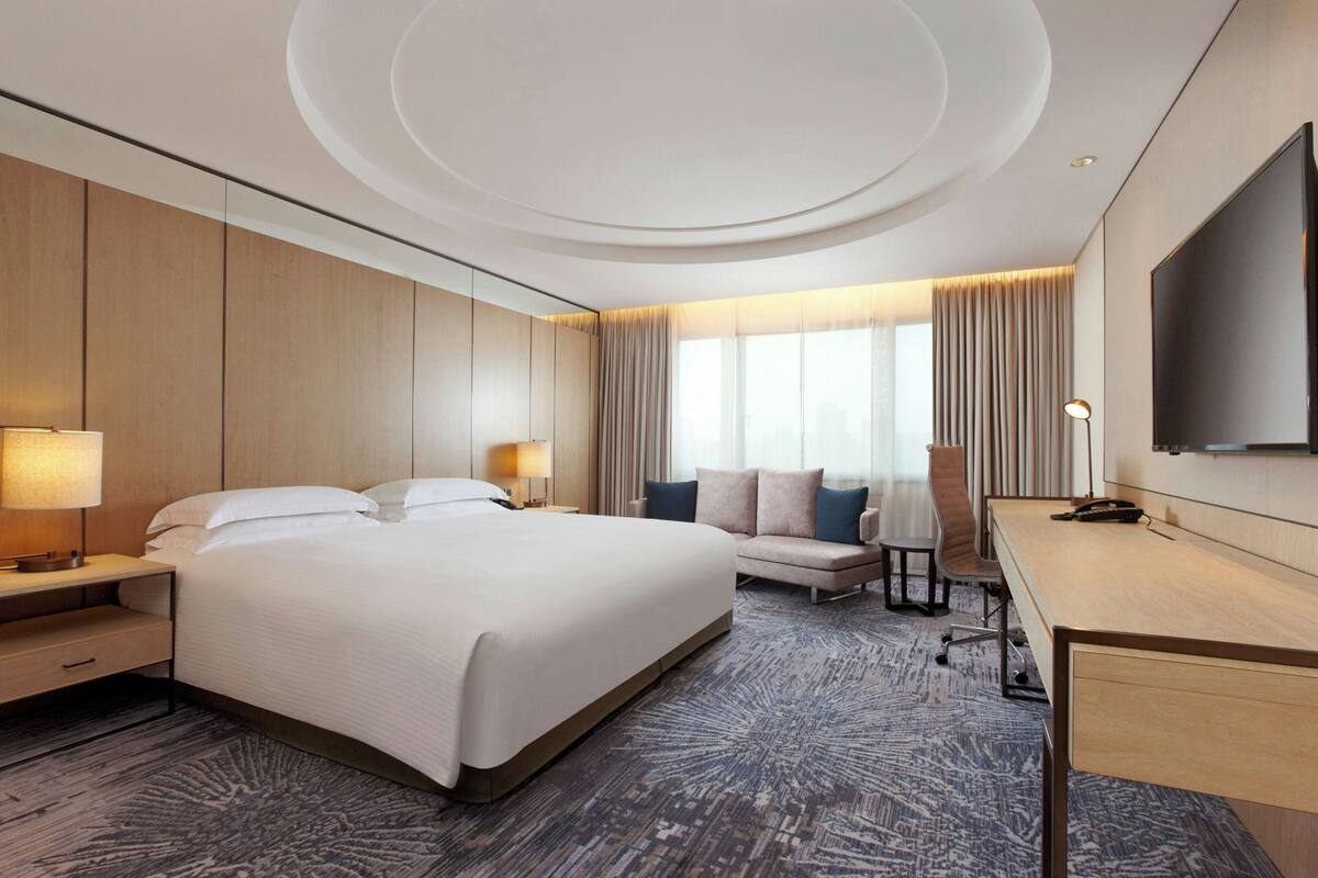 A modern hotel room with a large bed, a desk, a sofa, and a TV.