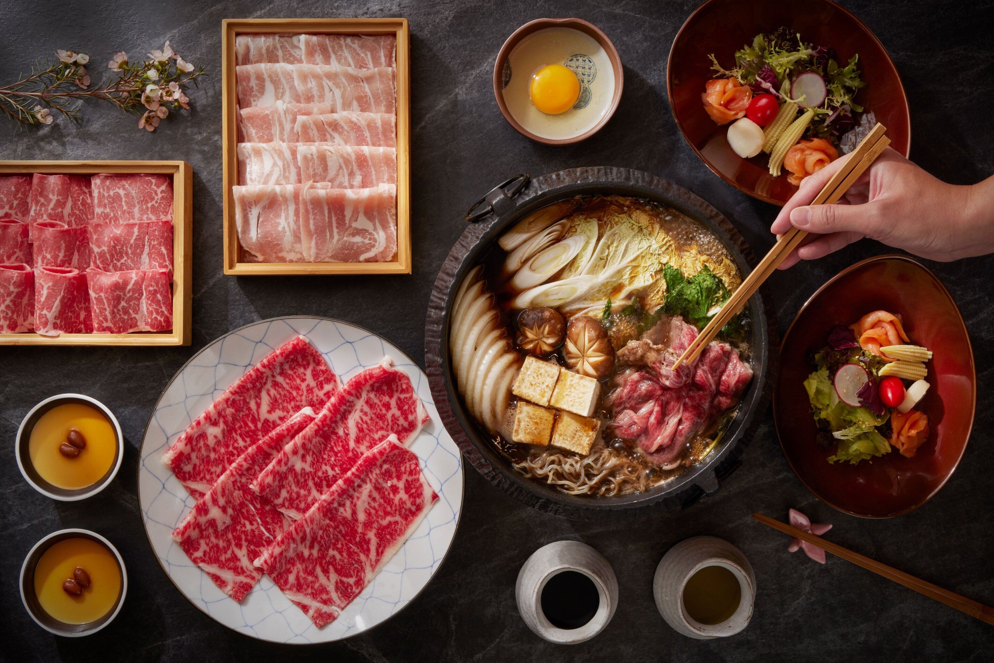 A variety of Japanese dishes including sashimi, tofu, and vegetables, arranged on a dark surface.