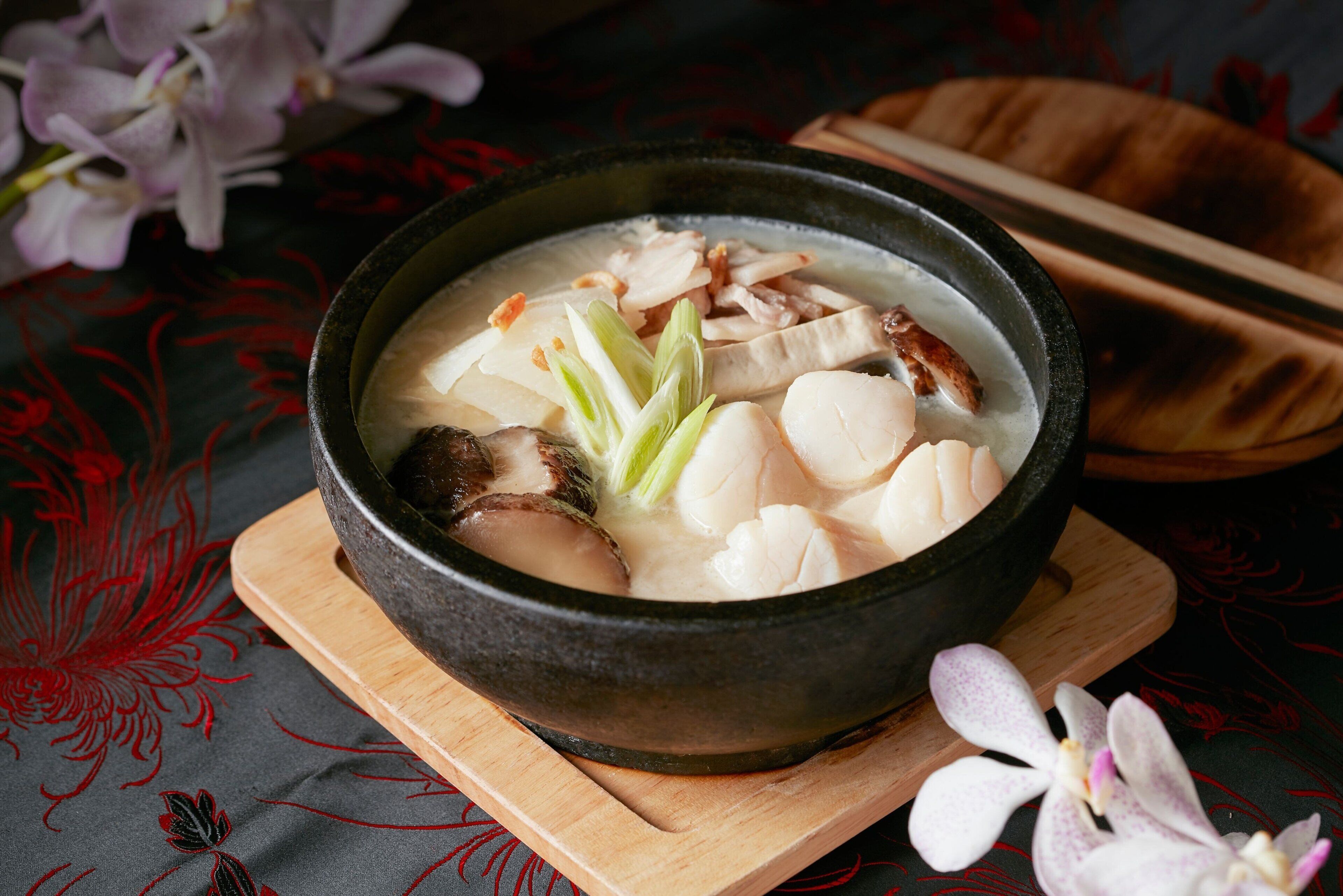 A bowl of soup with tofu and mushrooms on a wooden board.