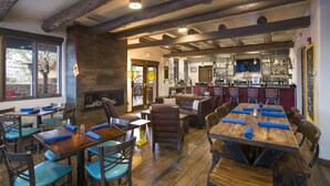 A restaurant with wooden tables and chairs, a bar area, and a fireplace. - The Sage Hotel (Santa Fe)