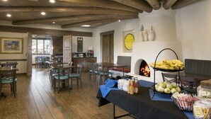 A dining area with wooden beams, tables, chairs, and a buffet table with food and drinks.