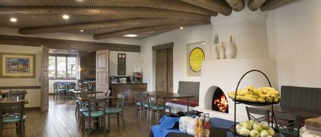 A dining area with wooden beams, tables, chairs, and a buffet table with food and drinks.