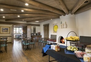 A dining area with wooden beams, tables, chairs, and a buffet table with food and drinks.