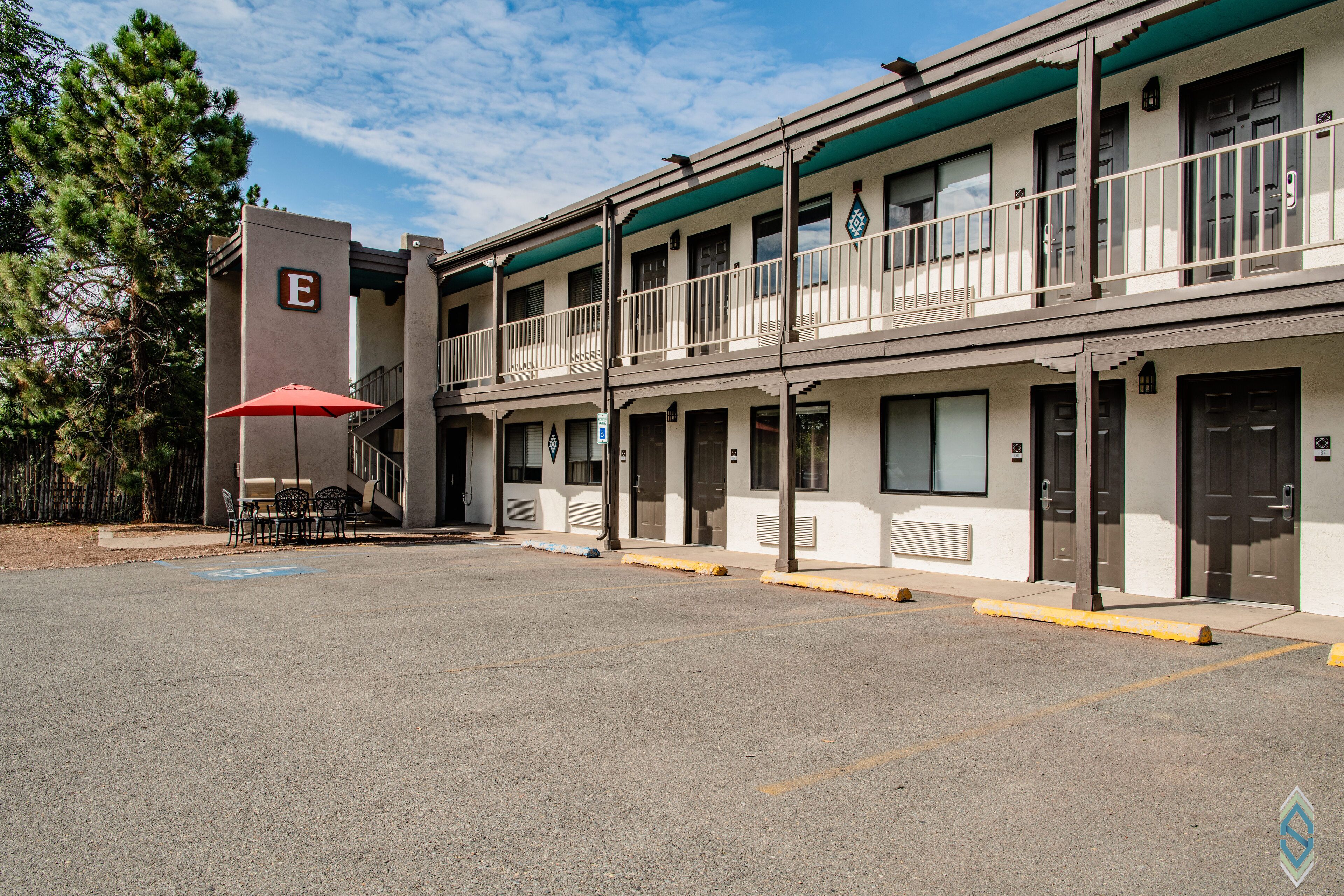 Un motel composé d’un bâtiment à deux étages, doté d’un espace extérieur avec des sièges et d’une zone abritée sous un parasol.