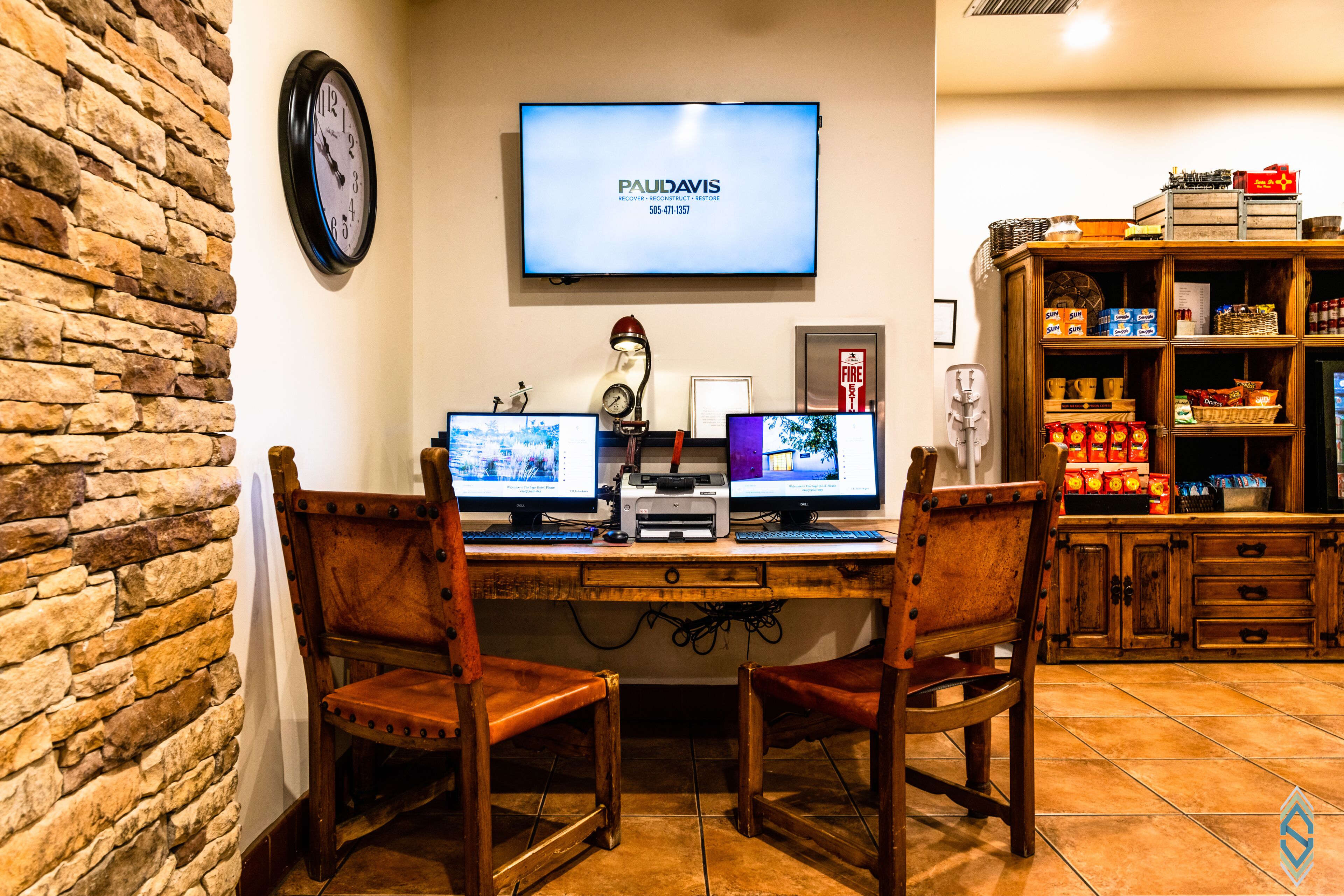 A workspace with two monitors, a clock, and a television displaying 'PAULDAVIS'.