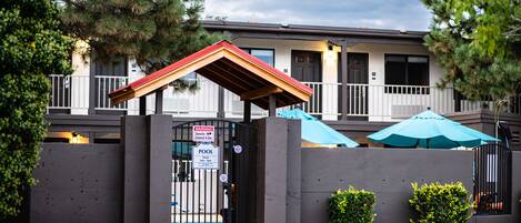 A gated entrance with a pool sign, a covered patio area, and a building with a balcony.