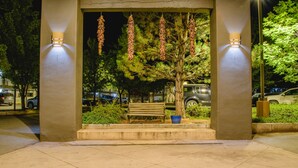 A covered outdoor seating area with a bench and a tree, illuminated by wall-mounted lights. - The Sage Hotel (Santa Fe)