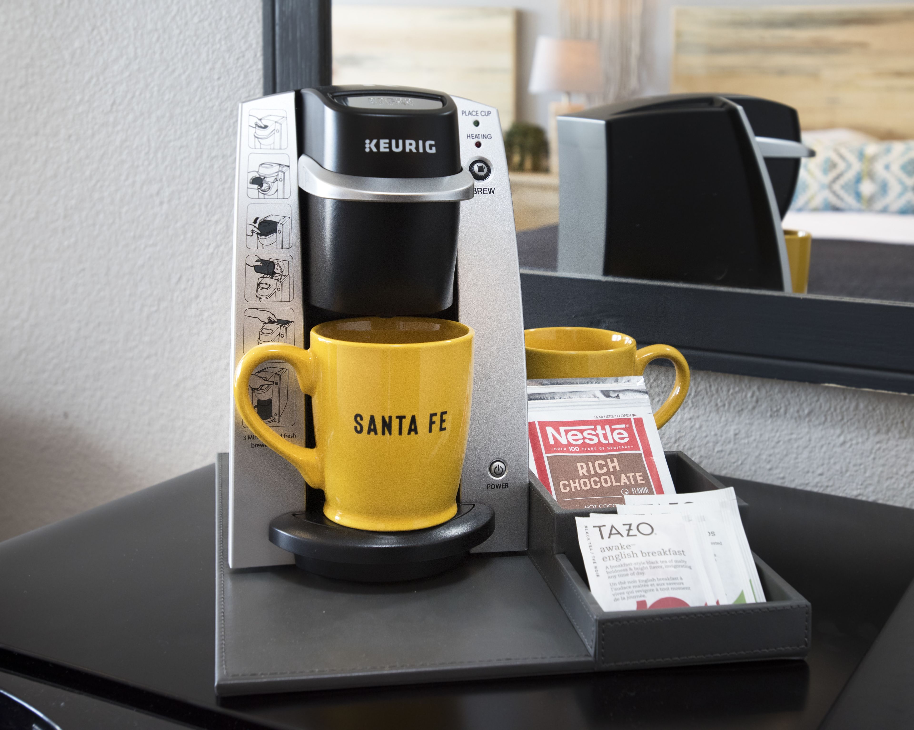 A Keurig coffee maker with a yellow mug labeled "Santa Fe" and a Nestle hot chocolate packet.