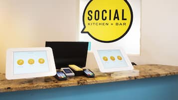 A counter with two tablets displaying a 'Stay-Touch' app interface, a cash register, and a 'Social Kitchen + Bar' sign.