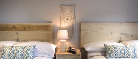 Una cama doble con un cojín estampado, una lámpara de noche y un teléfono sobre una mesita de madera.