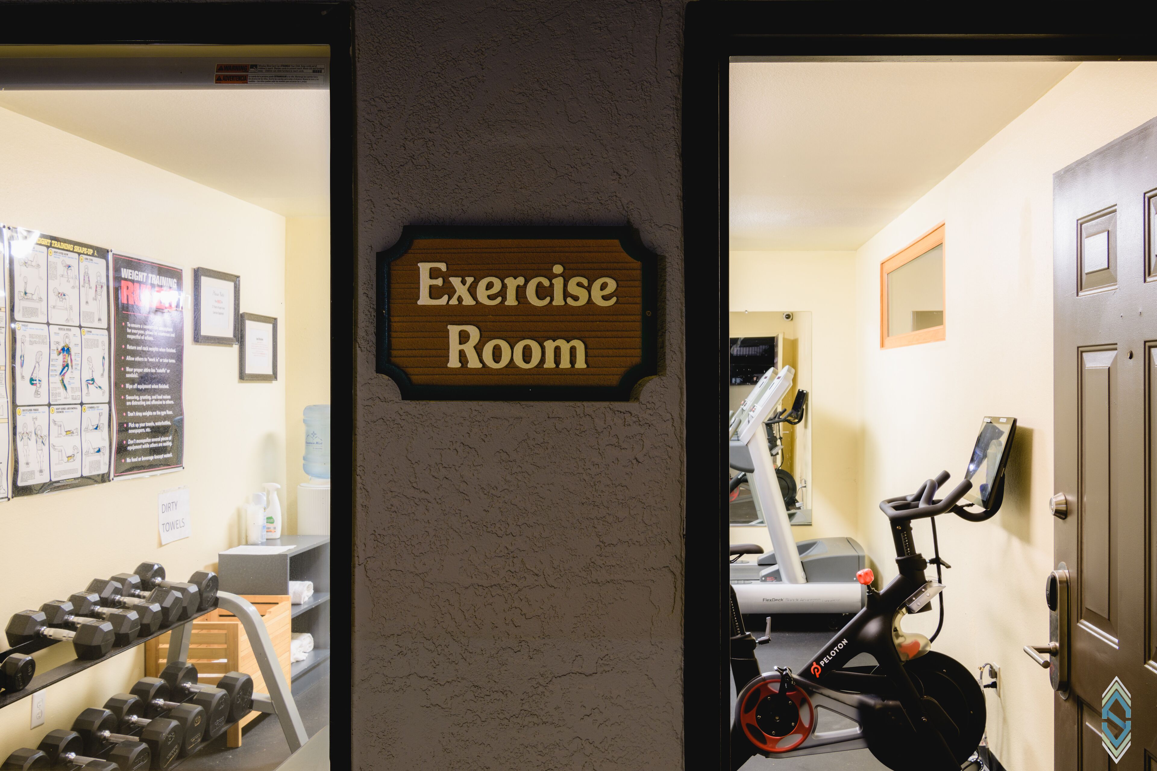 An exercise room with a sign, dumbbells, a treadmill, and an exercise bike.