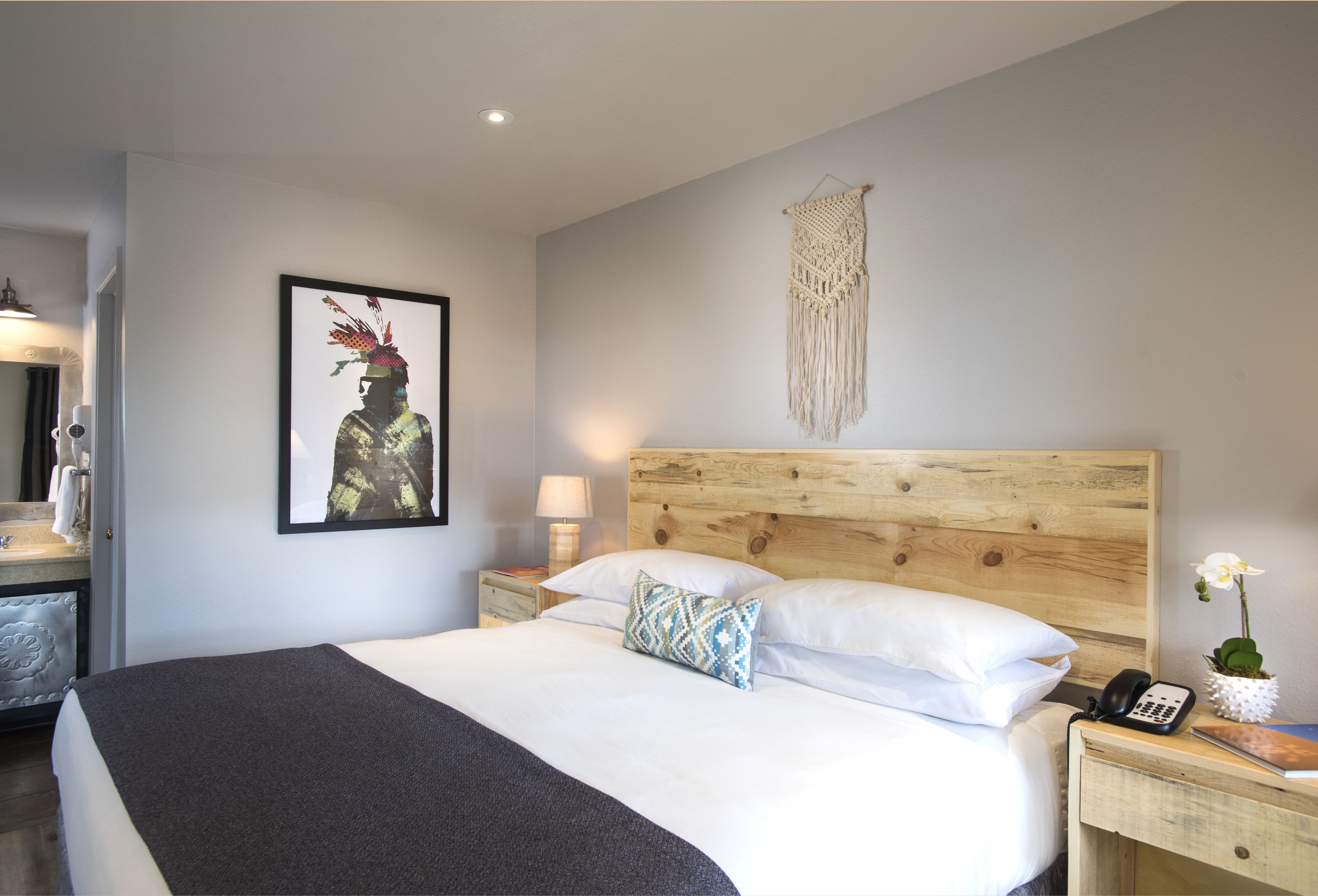 A neatly made bed with a wooden headboard, a bedside lamp, a phone, and a small vase with an orchid.
