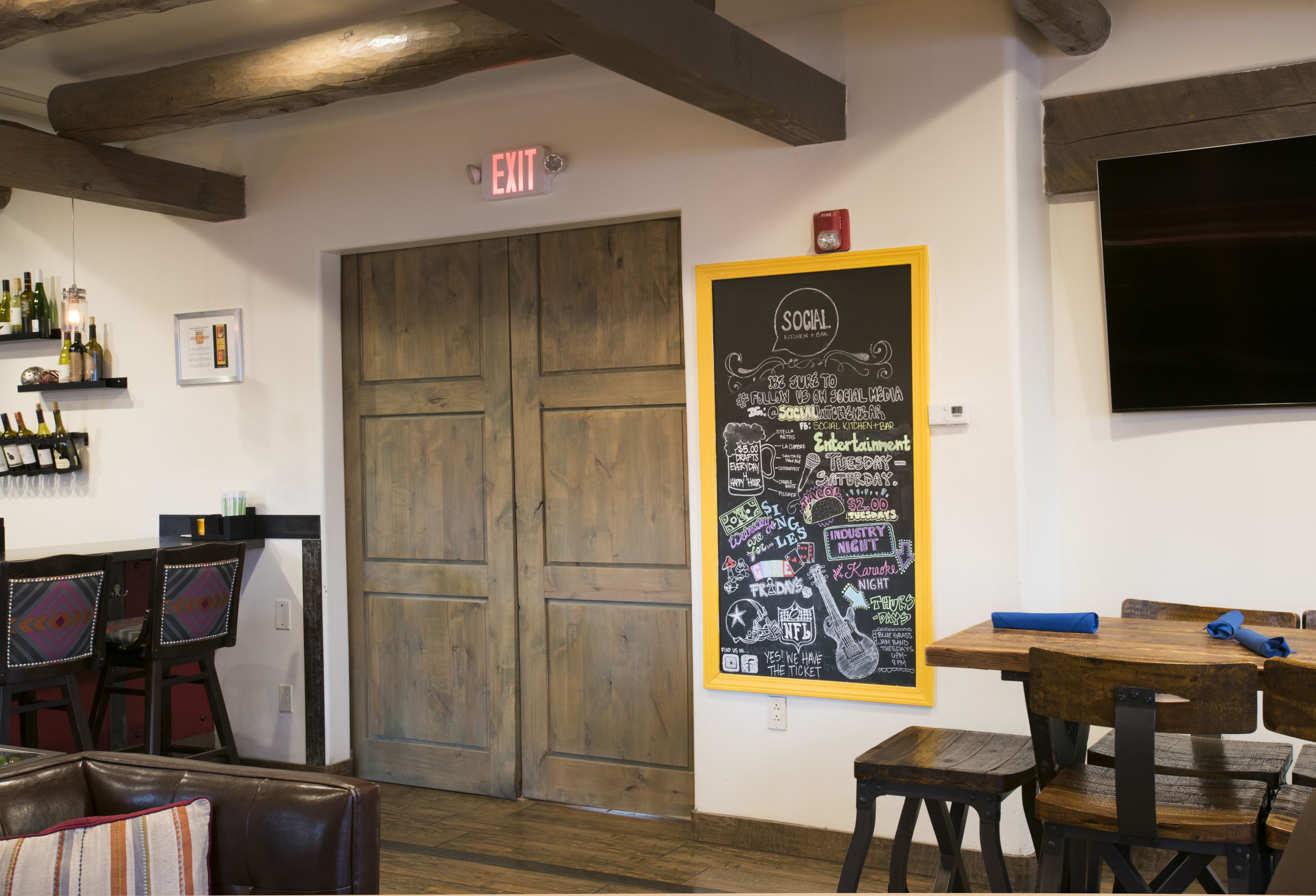A cozy restaurant interior with wooden furniture, a chalkboard menu, and a TV mounted on the wall.
