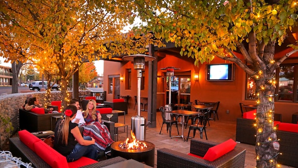 An outdoor seating area with wicker furniture, red cushions, and a central fire feature. - The Sage Hotel (Santa Fe)