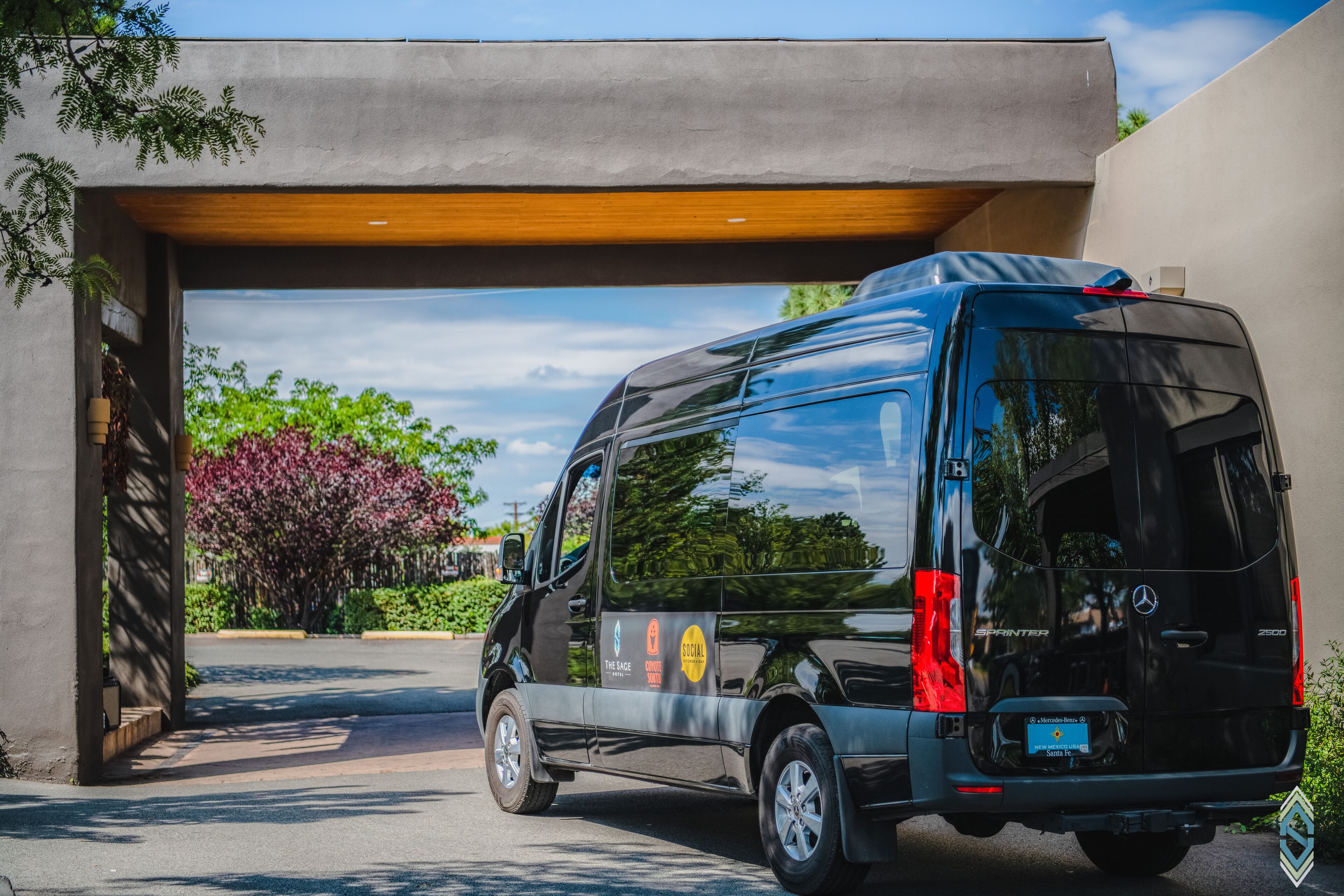 Un fourgon Mercedes-Benz Sprinter noir était garé sous un abri, d’où l’on pouvait admirer un jardin et des arbres.