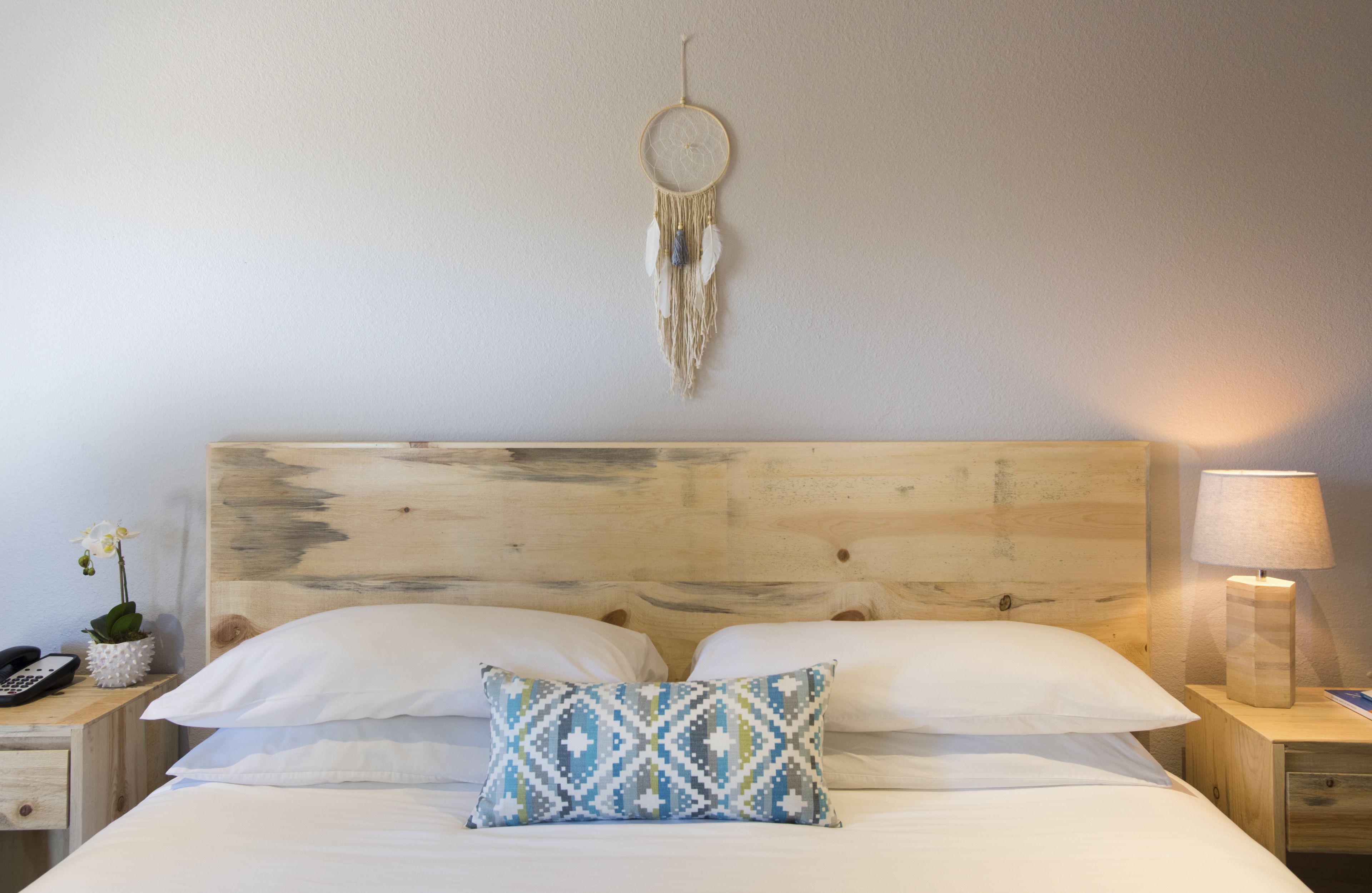A bed with white linens, a patterned pillow, and a dreamcatcher on the wall.